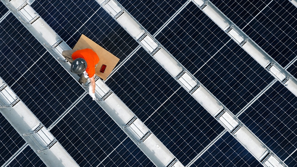Electrician inspecting commercial solar panel array from aerial view